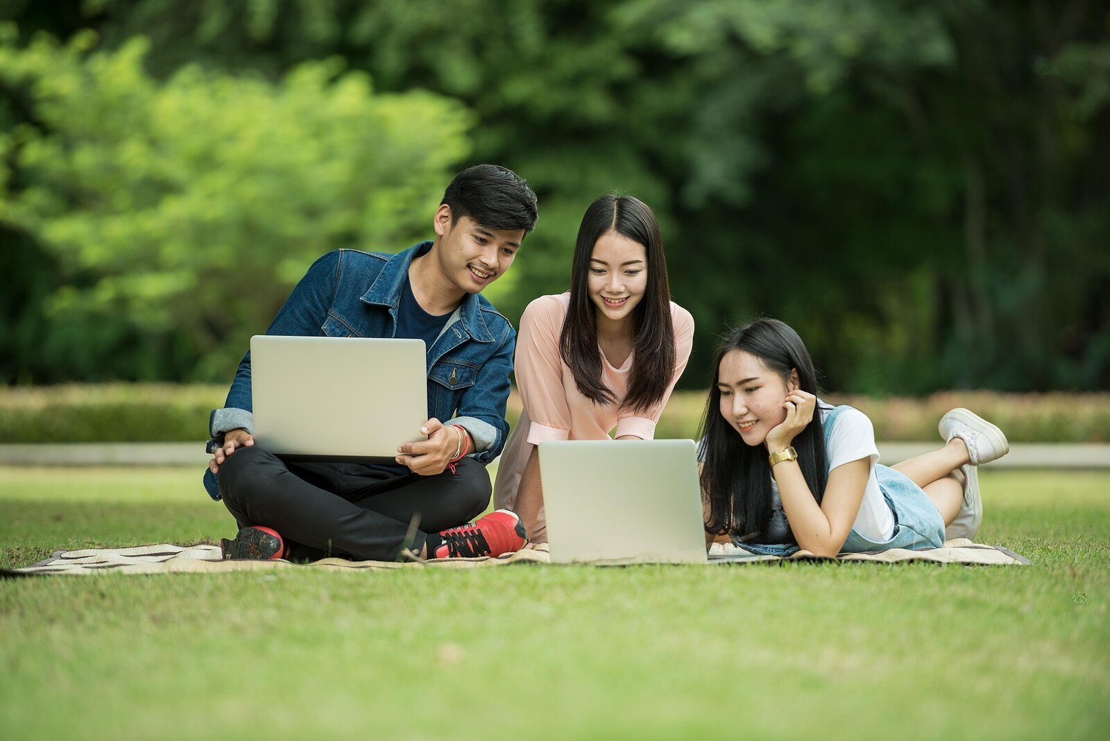 Tres estudiantes aprendiendo juntos al aire libre con sus portátiles