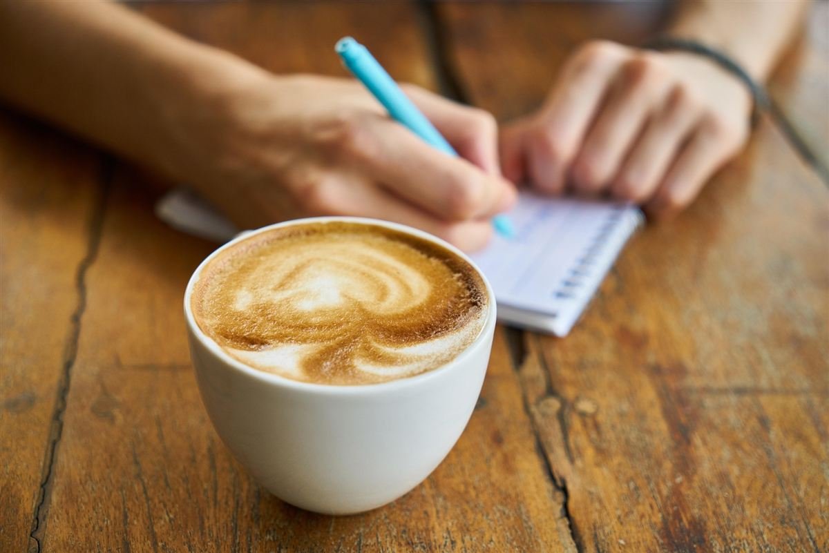 Mano escribiendo en una libreta con café